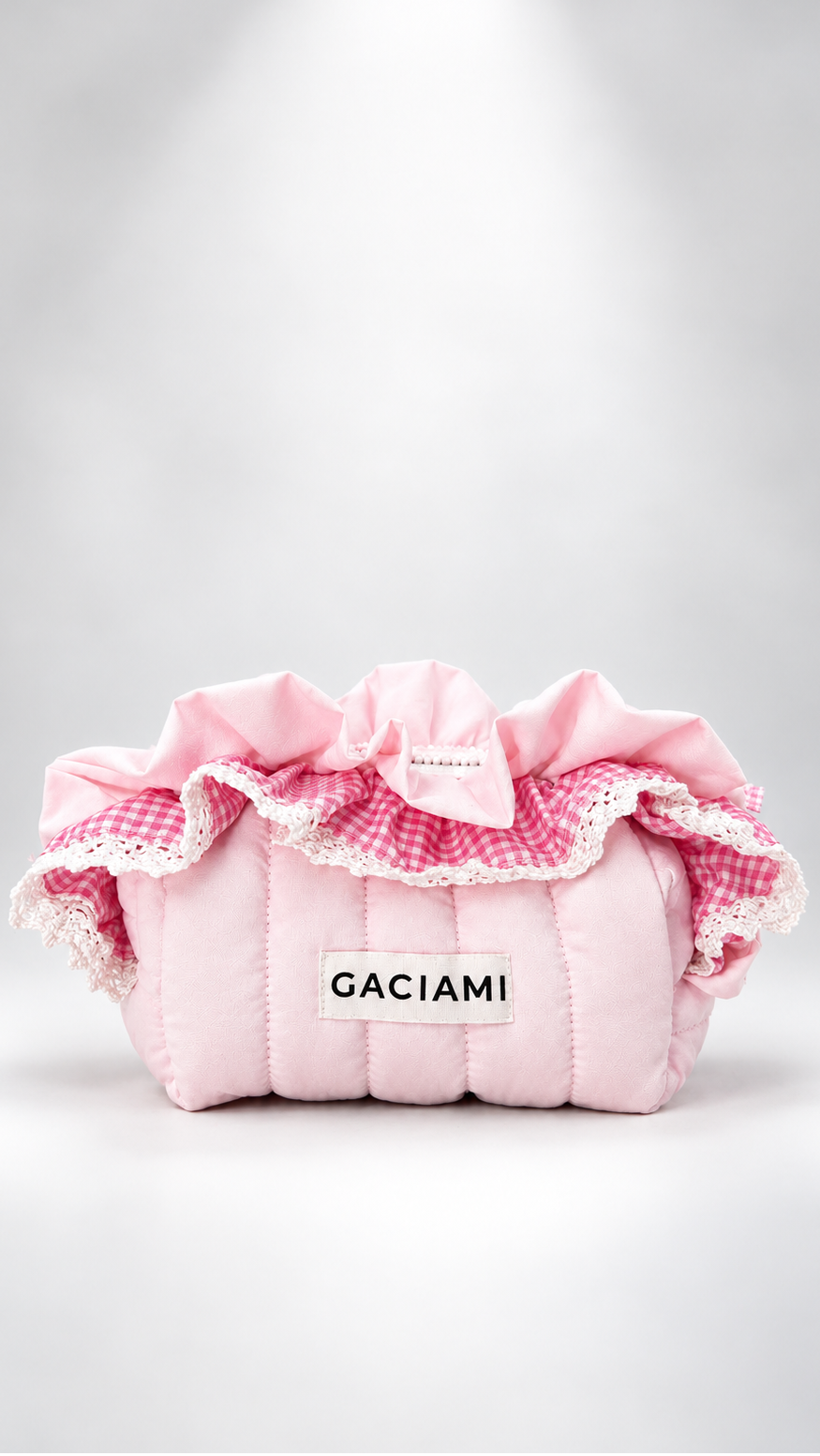 A pink quilted cosmetic pouch with ruffled trim, a bow, and a white label reading 'GACIAMI' on a light gray background.