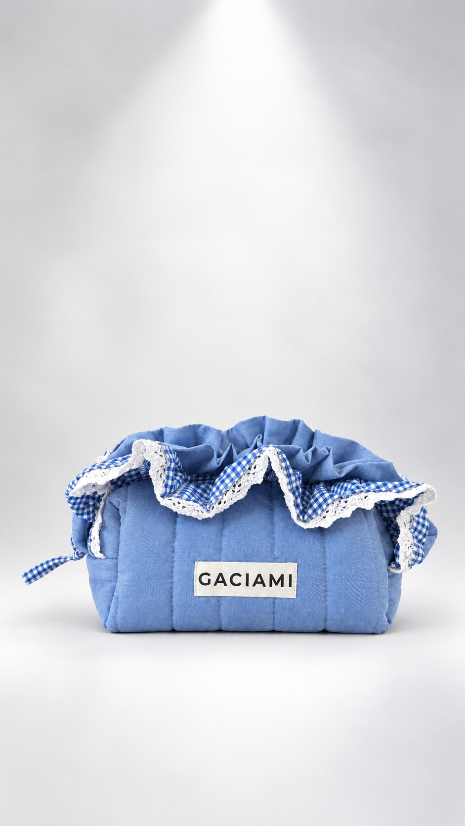 A light blue quilted fabric pouch with a drawstring closure, decorated with blue and white gingham ruffles and white lace trim. A white label on the front reads 'GACIAMI'.