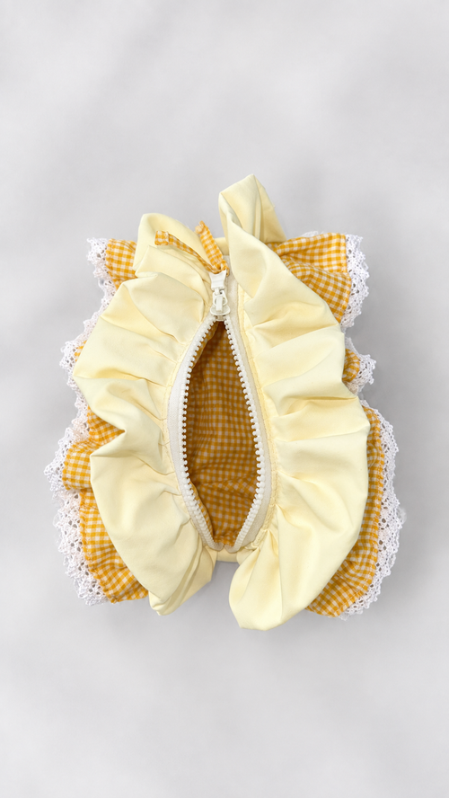 A small ruffled zippered pouch in pale yellow fabric with yellow-and-white gingham trim and white lace edges, photographed from above on a light gray background.