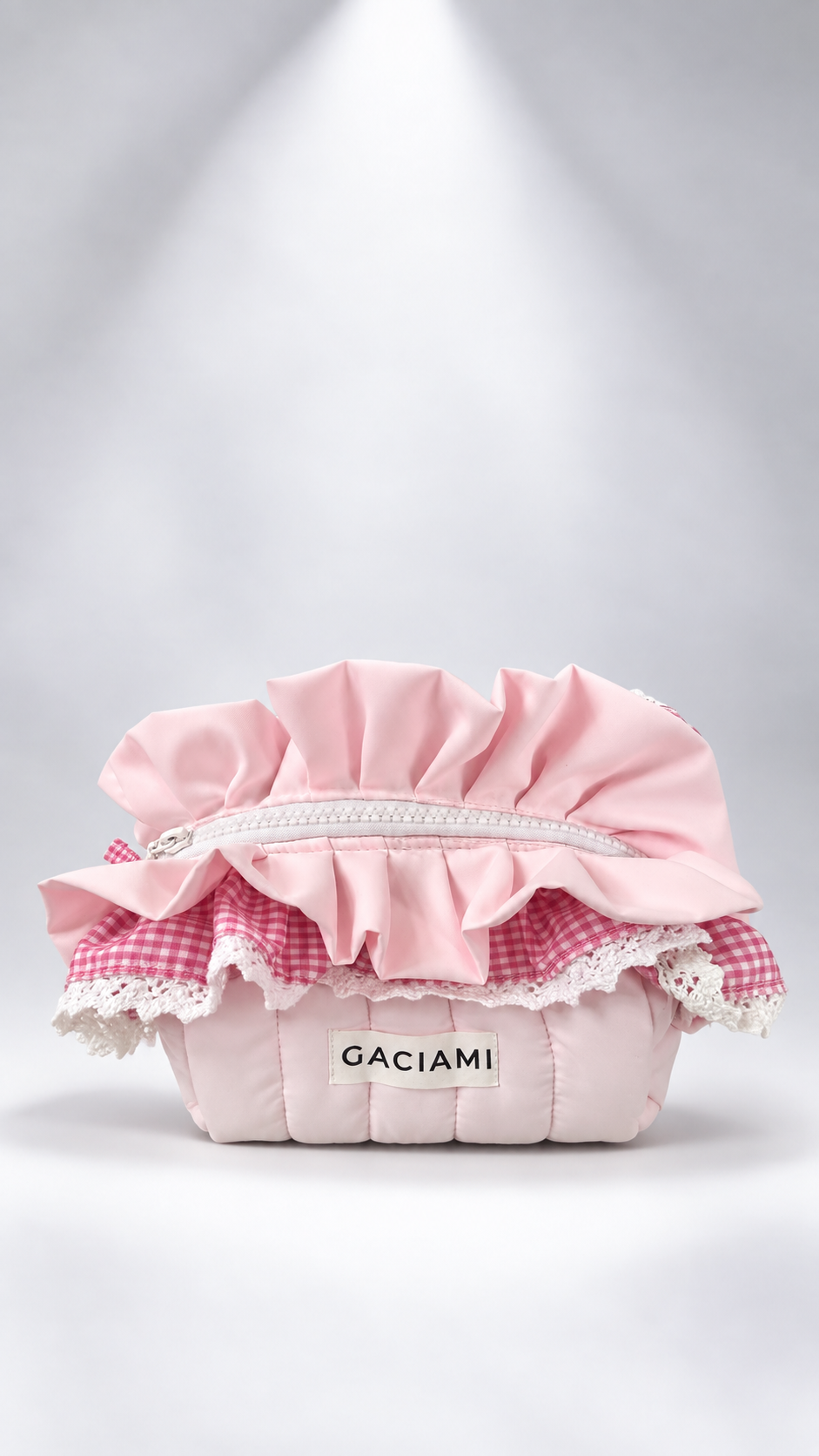 A pink quilted cosmetic pouch with ruffled trim, lace details, and a pink-and-white gingham fabric accent, featuring the brand name 'GACIAMI' on the front, set against a light gray background with a spotlight effect.