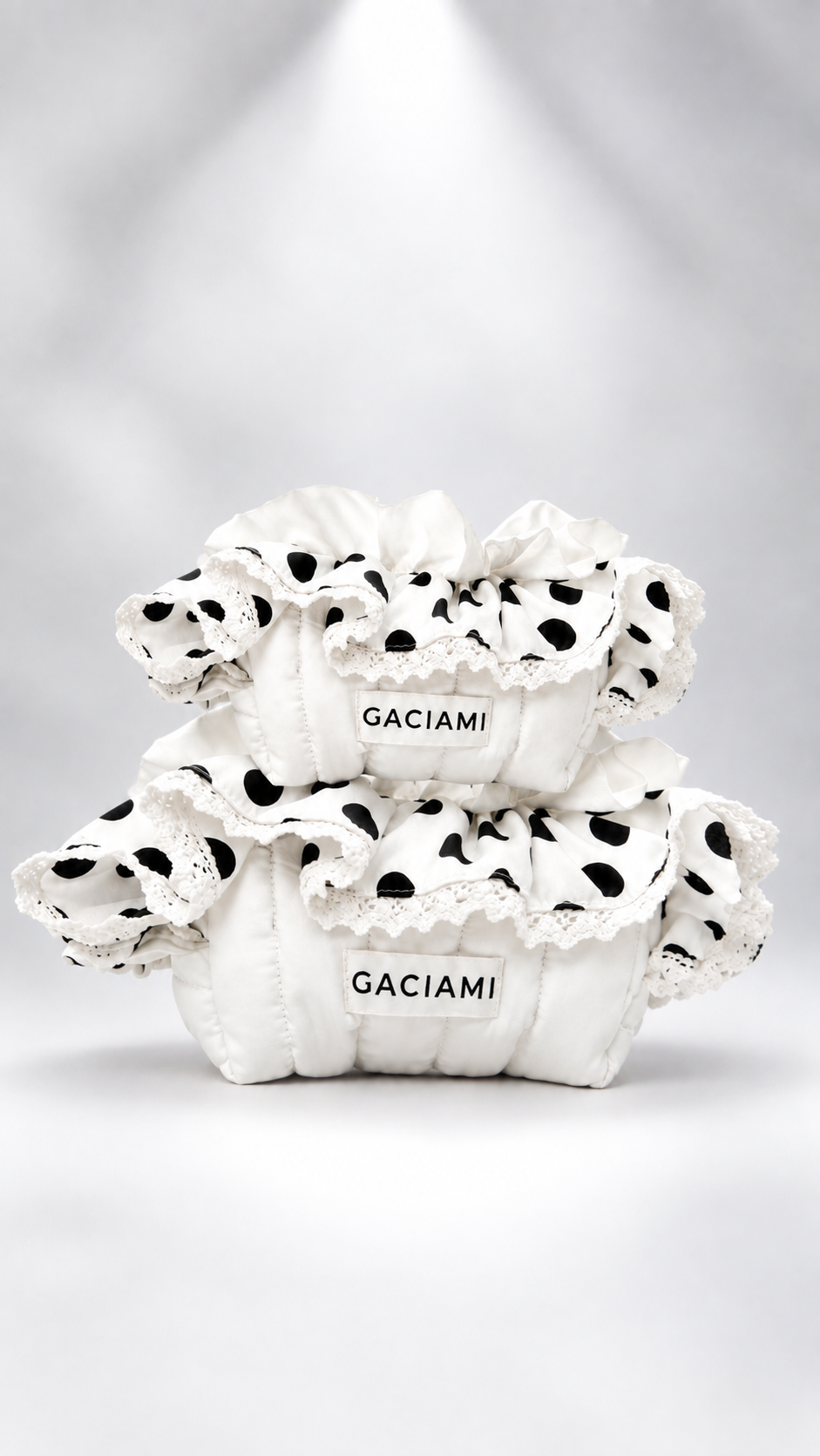 Two white ruffled pouches with black polka dots and lace trim, stacked on a light gray background. Each pouch has a white label reading 'GACIAMI'.