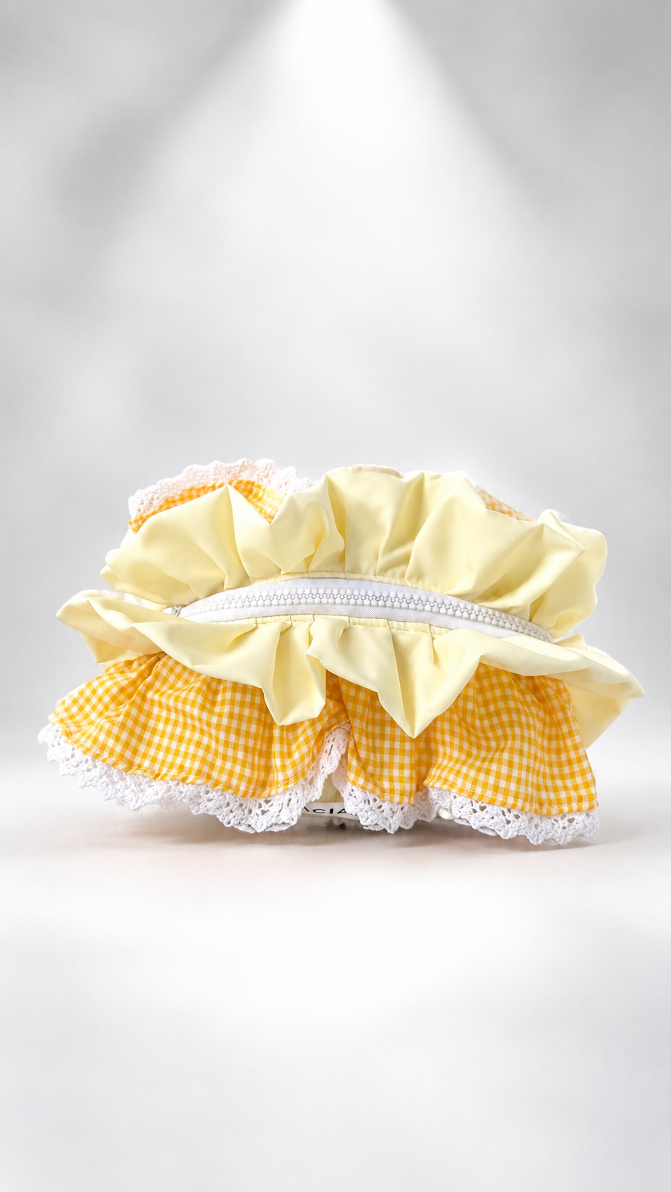 A yellow and white gingham ruffled headband with white lace trim and a white elastic band, photographed on a light gray background with a spotlight effect.