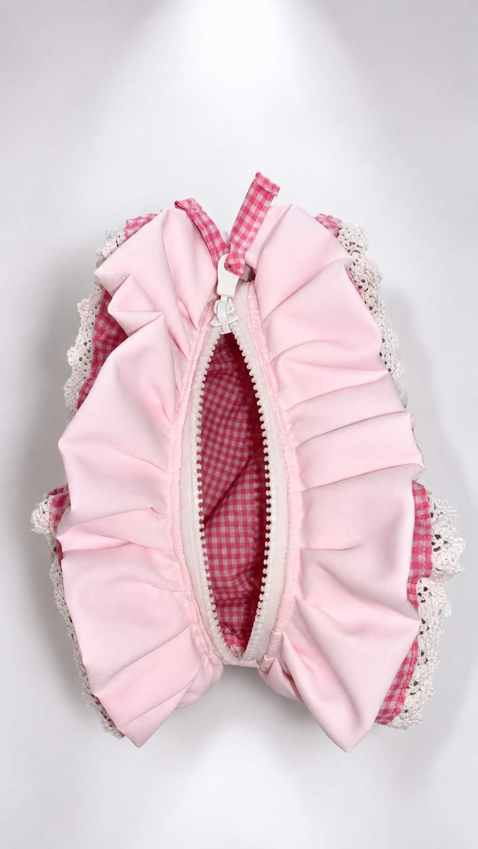 A pink ruffled zippered pouch with a pink and white gingham pattern, white lace trim, and a white zipper, shown on a light gray background.