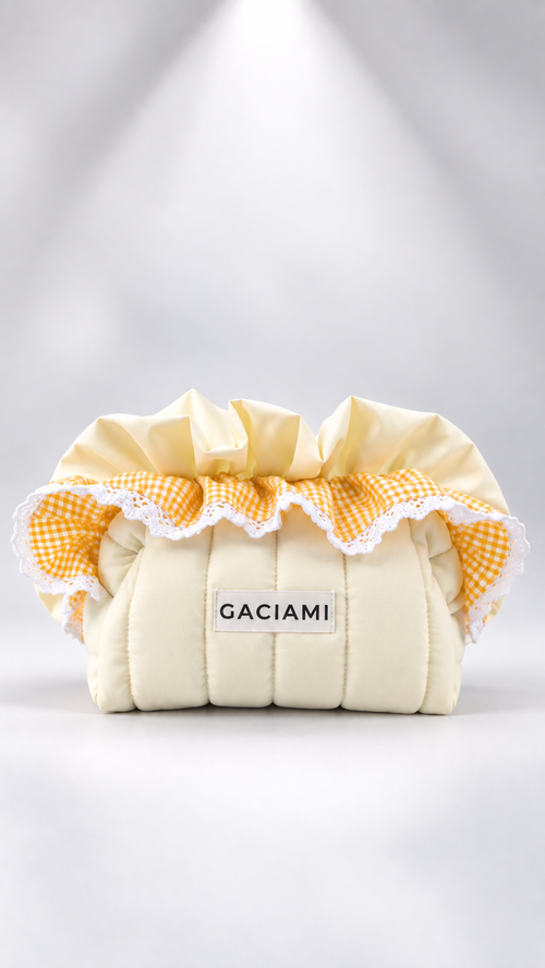 A cream-colored quilted fabric pouch or organizer with a ruffled yellow and white gingham trim and a white lace edge. A small white label on the front reads 'GACIAMI'.