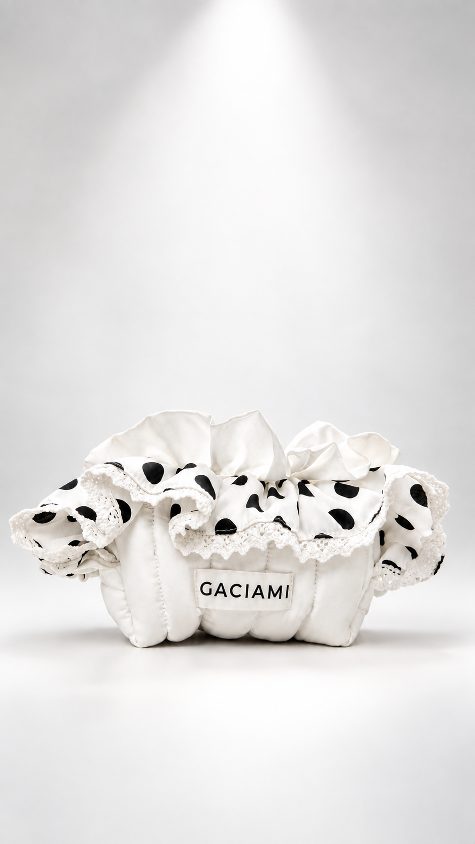 A white ruffled fabric bag with black polka dots and lace trim, featuring a white label that reads 'GACIAMI', set against a bright white studio background with a spotlight effect.