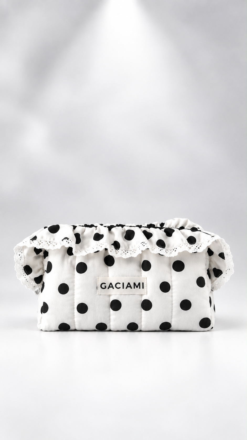 A white quilted cosmetic pouch with black polka dots, featuring a ruffled lace trim and a central label that reads 'GACIAMI'.
