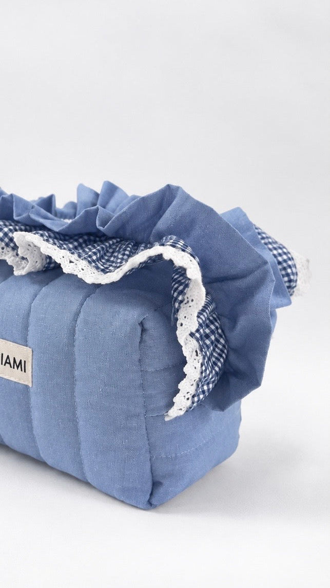 A light blue quilted fabric storage bag or organiser with a ruffled top trim, featuring a blue and white gingham check pattern and white lace trim. A small white label on the side reads 'GACIAMI'.
