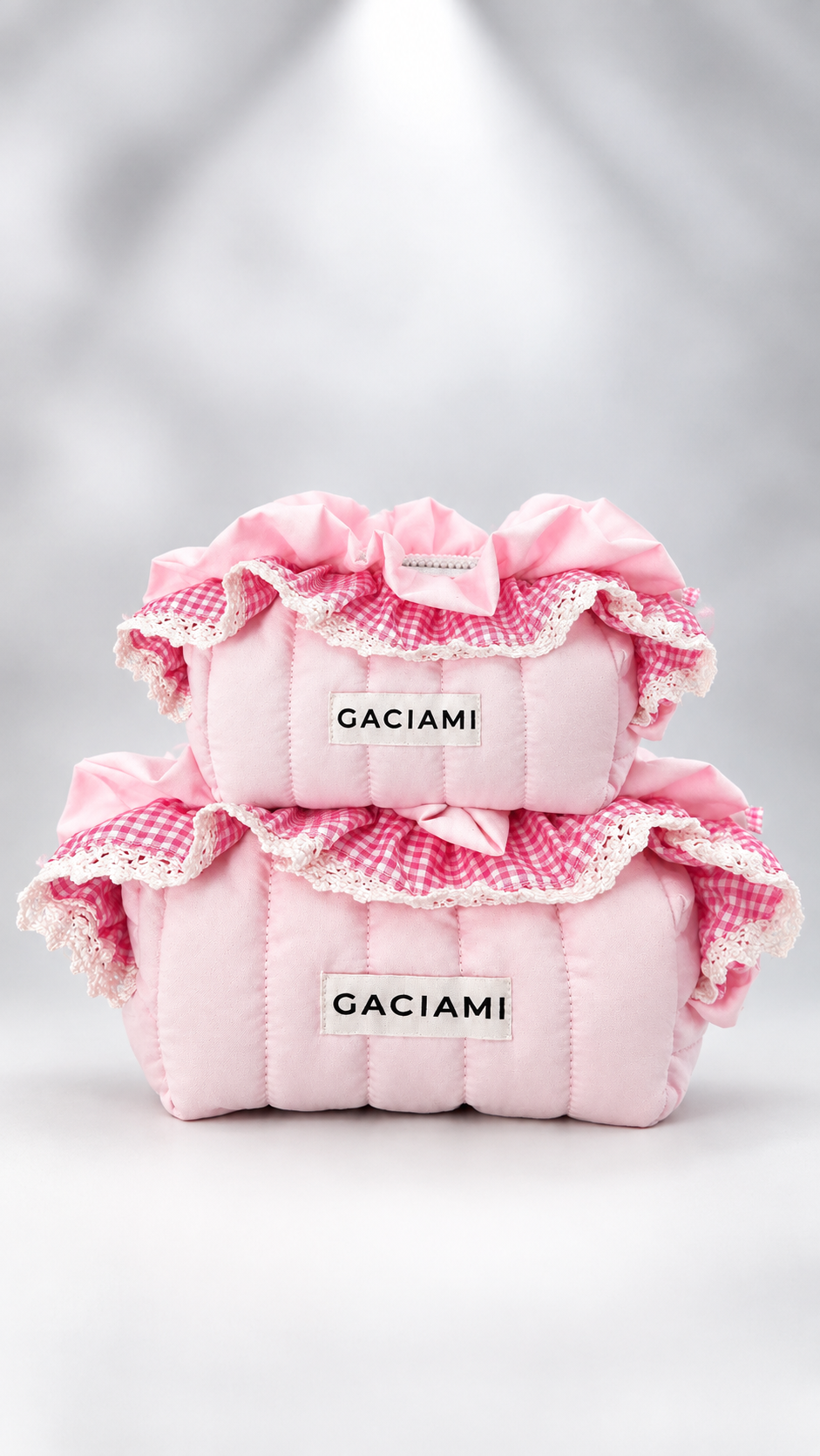 Two pink quilted cosmetic pouches stacked on a white surface, decorated with pink gingham ruffles, lace trim, and bows. The pouches feature a white label with the brand name 'GACIAMI' in black text.